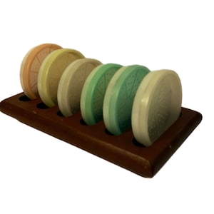 May include: A set of six vintage pastel-colored ceramic coasters with a decorative pattern, displayed in a wooden rack.