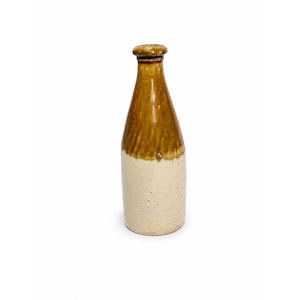 Peut inclure: Une grande bouteille en céramique présentant un design à deux tons. La partie supérieure et le goulot sont recouverts d'une glaçure brune brillante, tandis que le corps cylindrique inférieur est d'une couleur crème mate avec une texture légèrement mouchetée.