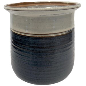 May include: A ceramic planter with a white rim and a blue and brown glaze. The planter has a rounded bottom and a wide opening.