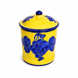May include: A cylindrical ceramic canister with a matching lid, featuring a bright yellow base color and hand-painted deep blue grape clusters and leaves. The lid has a small knob handle, and the entire piece is finished with blue trim.