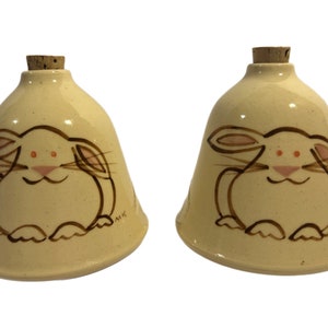 May include: Two ceramic salt and pepper shakers shaped like bells with a hand-painted design of a white bunny with pink ears and brown whiskers.
