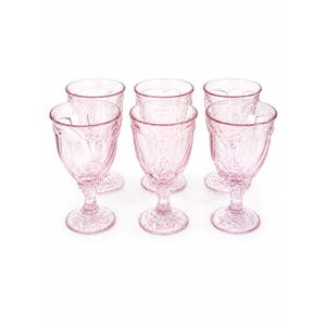 May include: A set of six light pink glass goblets featuring a textured, pressed pattern on the bowls and stems. Each goblet has a round base with a starburst design and a short, thick stem supporting a wide, rounded bowl with vertical ridges.