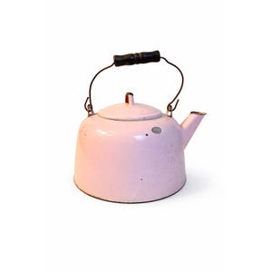 May include: A vintage pink enamel tea kettle with a black wooden handle and a spout. The kettle has a lid and a wire handle. The kettle is a light pink color and has some wear and tear.