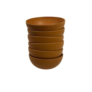 Pode incluir: Uma pilha de sete tigelas redondas castanhas. As tigelas têm um acabamento liso e fosco e um design simples e moderno. As tigelas são empilhadas ordenadamente umas sobre as outras, com a tigela superior ligeiramente inclinada.