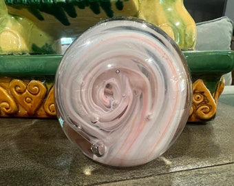Könnte beinhalten: Ein weißer Glas-Briefbeschwerer mit rosa und grauen Wirbeln und Luftblasen im Inneren.