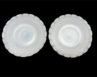 Può includere: Due piattini in ceramica bianca con bordo ondulato e design testurizzato in rilievo. I piattini sono vuoti.