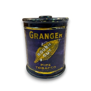 Könnte beinhalten: Eine Vintage-Dose Granger Rough Cut Pfeifentabak. Die zylindrische Dose hat einen dunkelblauen Hintergrund mit gelber Schrift und einem Blattdesign. Der Text enthält "Granger", "Rough Cut" und "Pipe Tobacco".