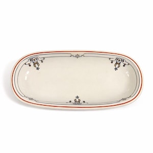 May include: An oval, off-white ceramic serving dish with a red and blue border. The dish features decorative floral and ribbon motifs in blue, gold, and black. The design is symmetrical, with the same pattern repeated at each end.