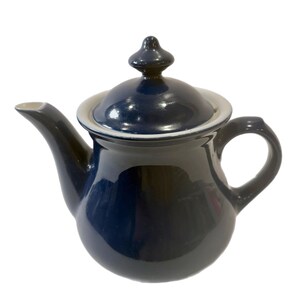 Może przedstawiać: Gliniany czajnik w ciemnoniebieskim kolorze z pokrywką i uchwytem. Czajnik ma biały rant wokół górnej krawędzi.
