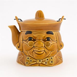Puede incluir: Tetera de cerámica marrón con forma de rostro de anciano sonriente. Incluye gafas, pajarita y tapa con asa pequeña. Detalles en negro para ojos y cejas. Diseño caprichoso y detallado.