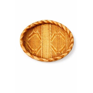 May include: Oval woven basket with a decorative diamond pattern in the center. The basket is made of light brown and tan natural fibers. The rim is a braided design, adding a textural element to the piece.