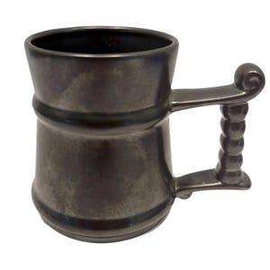 Puede incluir: Una jarra de cerveza de cerámica gris oscuro con un asa texturizada. La jarra tiene una base ancha y un cuerpo redondeado.