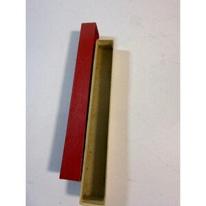 May include: An open, rectangular box with a beige interior and a separate, red, rectangular lid. The lid is a darker shade of red and has a textured surface. The box and lid are positioned on a white surface.