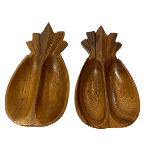 Puede incluir: Dos platos de servir de madera con forma de piña. Los platos están tallados en madera y tienen un color marrón natural. Cada plato tiene dos secciones.