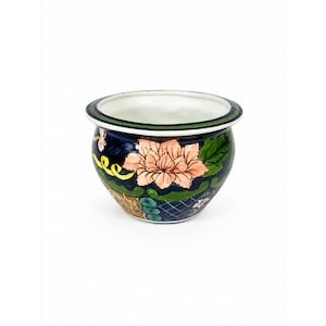 May include: A round ceramic planter featuring a dark blue base with a hand-painted peach-colored flower, green leaves, and yellow accents. The rim is decorated with a thin green and white border, and the interior of the bowl is white.
