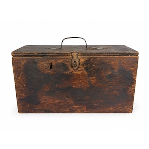 Puede incluir: Una caja de almacenamiento rectangular de madera con un acabado marrón oscuro desgastado. La caja cuenta con una tapa con bisagras, un asa de transporte de metal en la parte superior y un mecanismo de cierre central de metal con una cerradura.