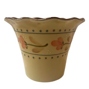 Puede incluir: Una maceta de cerámica amarilla con un borde festoneado y un diseño floral. La maceta tiene un borde marrón y un patrón de puntos azules y blancos.
