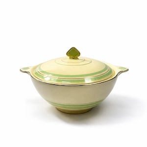 Op de afbeelding: Crèmekleurige keramische serveerschaal met deksel. De kom heeft groene horizontale strepen en gouden randen. Het deksel heeft een groene ruitvormige handgreep. De kom heeft twee kleine handvatten aan weerszijden.
