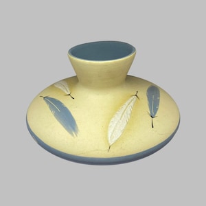 May include: A light yellow ceramic vase with a wide base and a narrow neck. The vase is decorated with blue and white feathers.
