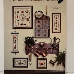 Op de afbeelding: Een cross-stitch sampler patroonboekje met keukenantiek. De omslag toont verschillende cross-stitch ontwerpen, waaronder een theepot, een kruidenrek en een plank met mokken. De tekst op de omslag luidt "Kitchen Antiques Sampler" en "Helene Halverson Designs".