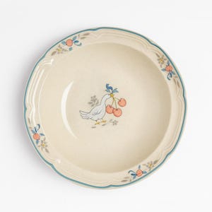Może przedstawiać: Kremowy ceramiczny talerz z niebieską obwódką i falistą krawędzią. Talerz przedstawia ilustrację gołębia trzymającego wiśnie, z kwiatowymi i owocowymi akcentami. Dekoracyjny element do serwowania potraw.