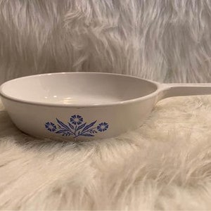 May include: White ceramic baking dish with a blue floral design. The dish has a handle on one side.