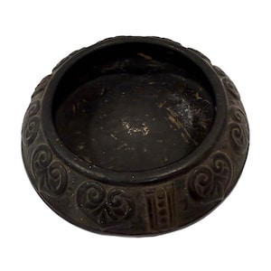 Puede incluir: Un cuenco de cerámica negro con intrincados diseños florales alrededor del borde. El cuenco está vacío y tiene una superficie lisa, ligeramente desgastada.
