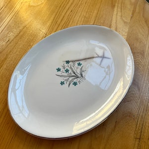 Könnte beinhalten: Weiße ovale Servierplatte mit goldfarbenem Rand und einem floralen Design in Grün- und Blautönen.
