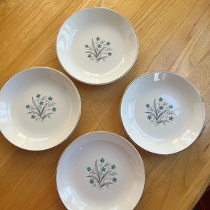 May include: Four white ceramic bowls with a gold rim and a floral design featuring teal blue flowers and gray leaves.