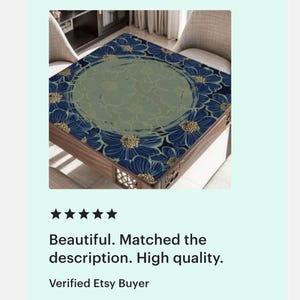 Op de afbeelding: Vierkante houten tafel met een bloemenontwerp. Het tafelblad heeft een marineblauw bloemenpatroon met gouden accenten langs de randen en een centraal groen bloemenontwerp. De tafel heeft een donkerhouten frame.