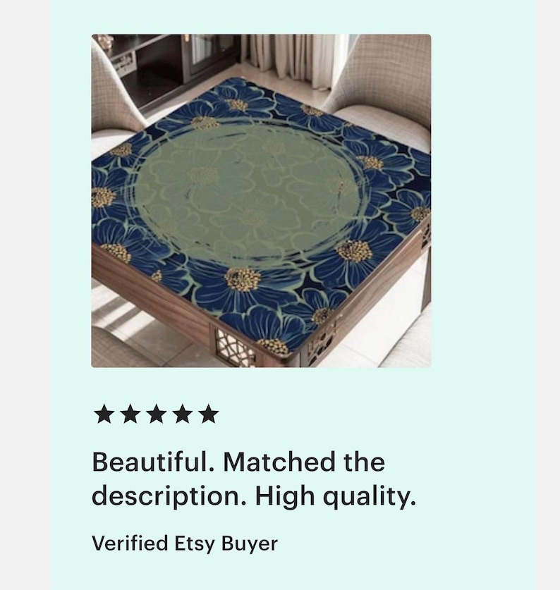 Op de afbeelding: Vierkante houten tafel met een bloemenontwerp. Het tafelblad heeft een marineblauw bloemenpatroon met gouden accenten langs de randen en een centraal groen bloemenontwerp. De tafel heeft een donkerhouten frame.