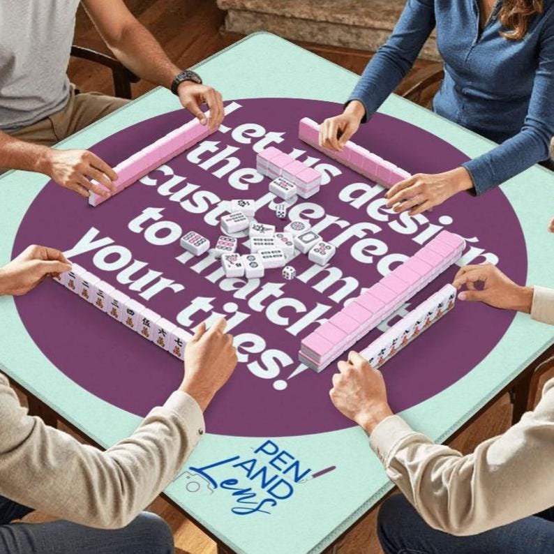 May include: A square mahjong table with a light green surface and a large purple circle in the center. The table has the text "Let us design the perfect to match your tiles!" in white. Pink mahjong tiles are arranged around the table.
