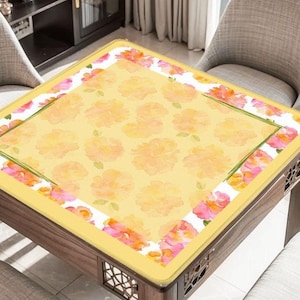 May include: A square table with a yellow floral patterned top. The table has a border of pink and orange flowers on a white background. The table is made of wood and has decorative cutouts on the sides.