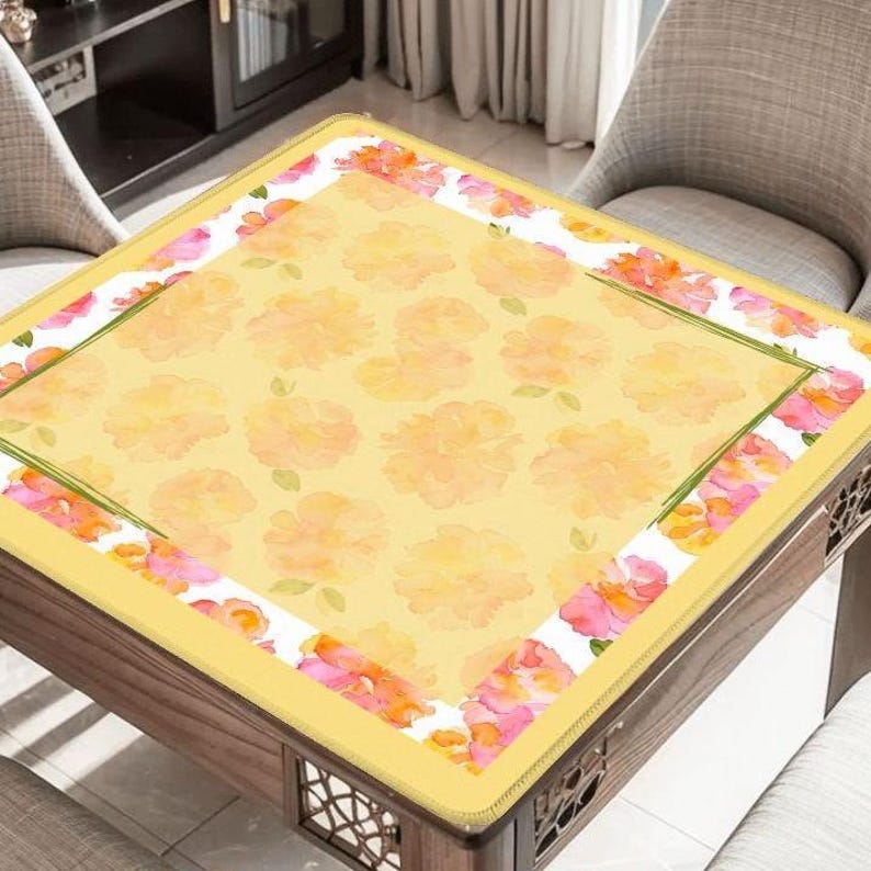 May include: A square table with a yellow floral patterned top. The table has a border of pink and orange flowers on a white background. The table is made of wood and has decorative cutouts on the sides.