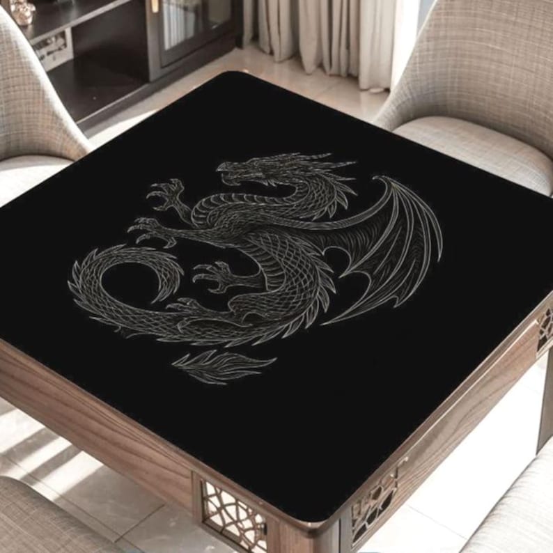 May include: A square, wooden table with a black top featuring a detailed, silver dragon design. The dragon is depicted with wings and a coiled body. The table has a dark wood frame and is surrounded by neutral-toned chairs.