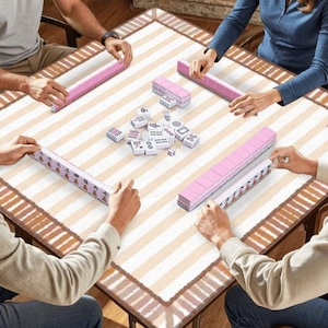 Pu&ograve; includere: Una partita di mahjong in corso, con giocatori attorno a un tavolo quadrato. Il tavolo ha un motivo a strisce beige e bianco. Sono visibili rastrelliere e tessere rosa, insieme a tessere e dadi bianchi. I giocatori tengono in mano le tessere.