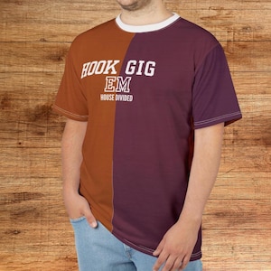 May include: A two-toned t-shirt with a white collar. The left side is a burnt orange color, and the right side is a deep purple. The text "HOOK GIG EM" is printed in white, with "HOUSE DIVIDED" below it.