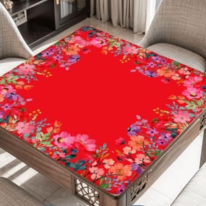 May include: A square table with a vibrant red surface, adorned with a floral border featuring pink, purple, and orange blooms. The table has a wooden frame and is set in a room with chairs.