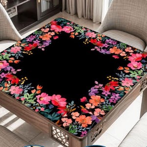 May include: A square table cover featuring a solid black center bordered by a vibrant floral pattern. The design includes watercolor-style flowers in shades of pink, red, orange, and purple, accented with green leaves and small yellow buds.
