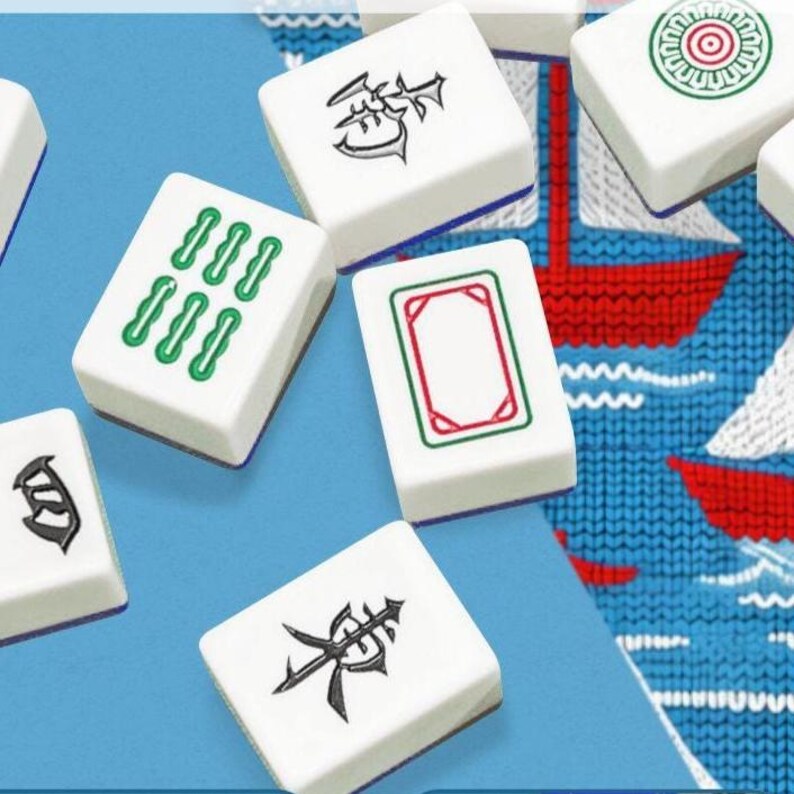 May include: White Mahjong tiles with various symbols and markings in green and black. The tiles are scattered on a blue surface with a patterned background featuring red and white boat designs. A classic game.