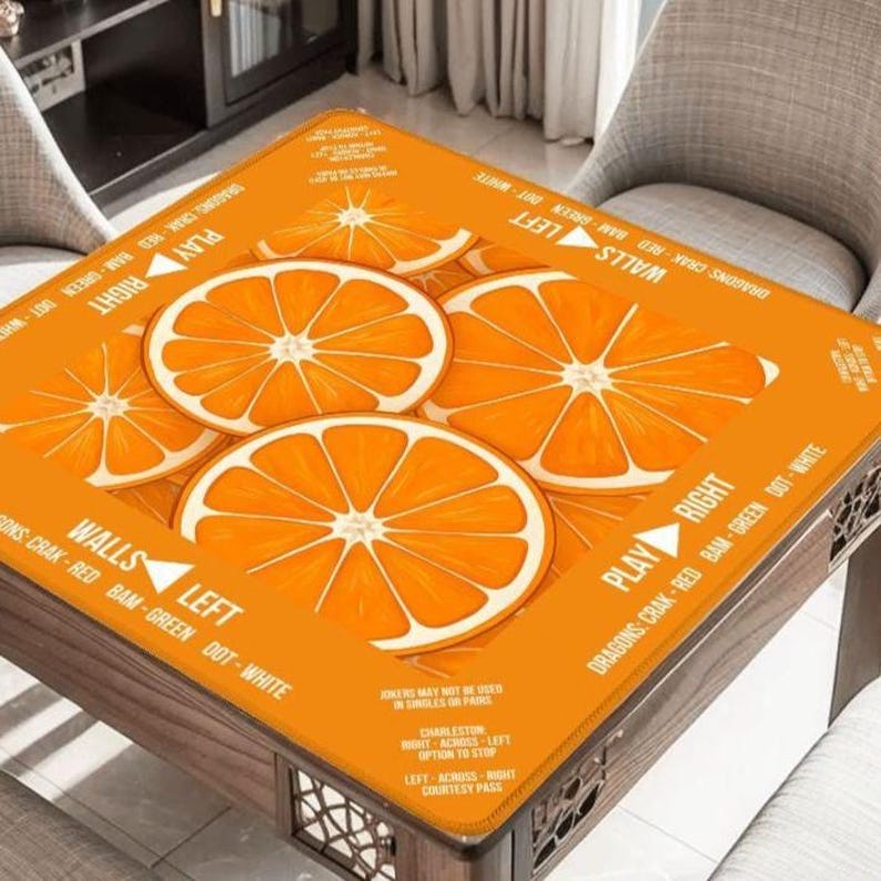 K&ouml;nnte beinhalten: Eine orangefarbene Tischdecke mit einem Design aus Orangenscheiben. Die Decke tr&auml;gt die Aufschrift "PLAY RIGHT" und "WALLS LEFT". Die Tischdecke liegt auf einem Holztisch.