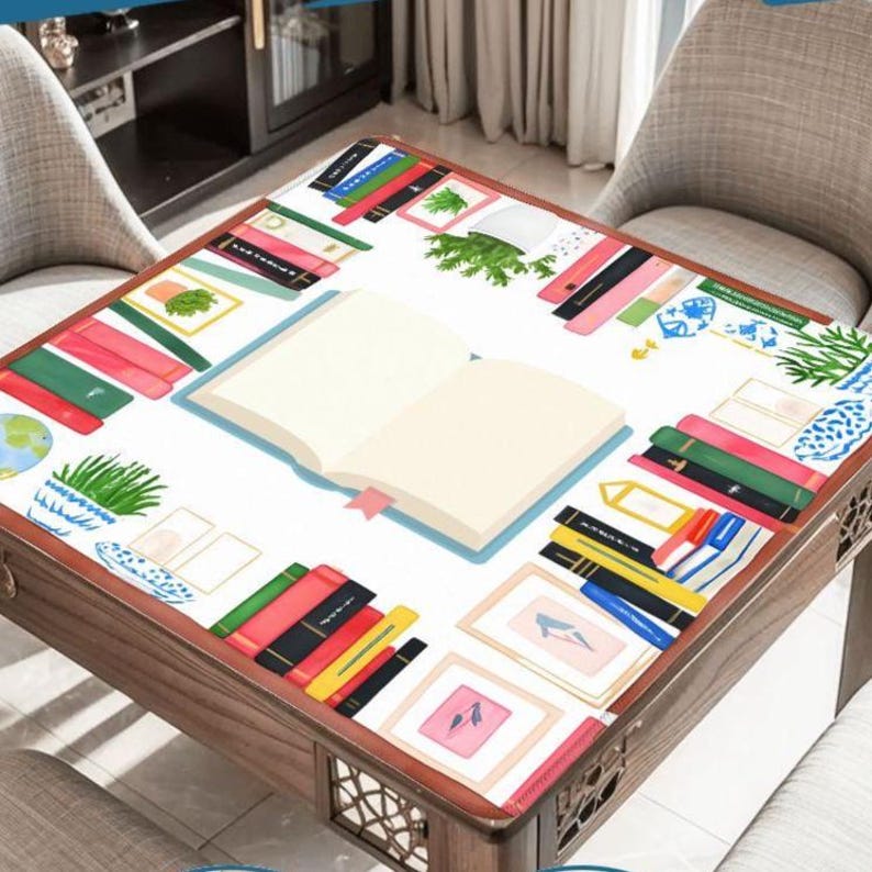 May include: A square wooden table with a white surface featuring a colorful book and art design. The table's surface is decorated with illustrations of books, framed pictures, and plants. The table has a dark brown wooden frame and decorative cutouts on the sides.