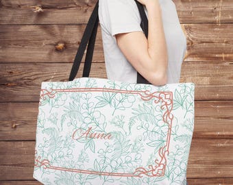 May include: White tote bag with a botanical design in green and coral. The bag features a floral pattern with the name "Auna" in cursive script within a coral-colored frame. Black straps complete the design.