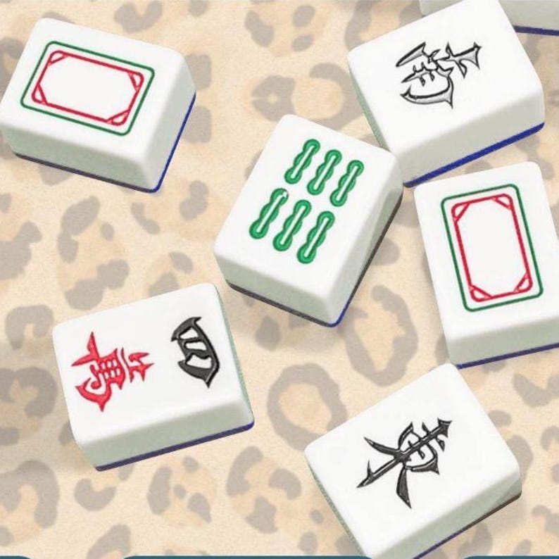 Pode incluir: Pe&ccedil;as brancas de Mahjong com v&aacute;rios s&iacute;mbolos e n&uacute;meros em verde e vermelho. As pe&ccedil;as t&ecirc;m uma borda azul e est&atilde;o dispostas sobre um fundo com estampa de leopardo. As pe&ccedil;as s&atilde;o para o tradicional jogo de tabuleiro.