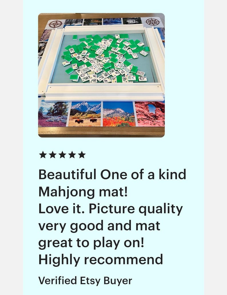 May include: A Mahjong game set with green tiles scattered on a light blue mat, framed by a white wooden border. The mat rests on a decorative surface with landscape images. The text on the image says: Beautiful One of a kind Mahjong mat!