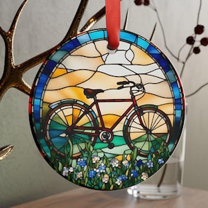 May include: Round stained glass ornament featuring a bicycle design. The bicycle is red with black tires, set against a landscape of yellow, blue, and green. A red ribbon is attached for hanging.