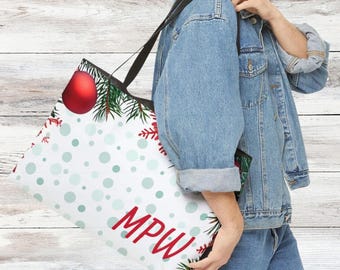 May include: A white tote bag with a Christmas theme, featuring red ornaments, green pine needles, and snowflakes. The bag has a pattern of light blue polka dots and the red letters "MPW". The bag has a black shoulder strap.