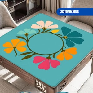 May include: A square table with a teal floral design. The design features colorful flowers in pink, orange, teal, and white, arranged around a central circle. The table is made of wood and has a decorative pattern on the sides. The word "CUSTOMIZABLE" is in a blue rectangle.