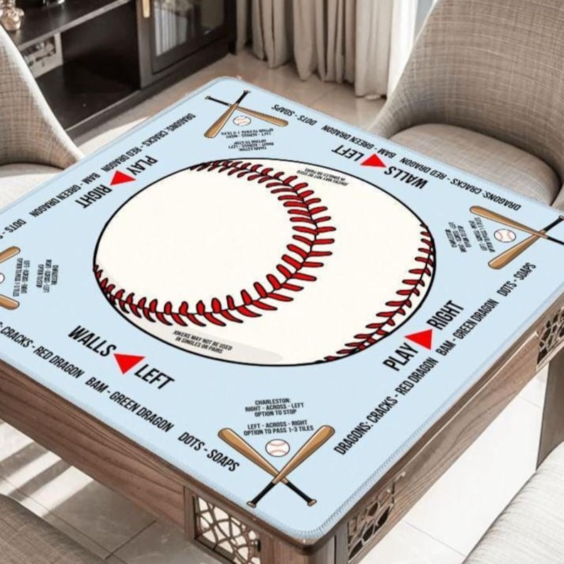May include: A square light blue table mat featuring a large central baseball with red stitching. The mat includes printed text and graphics of crossed baseball bats, with directional arrows and labels like PLAY RIGHT, WALLS LEFT, and game rules.