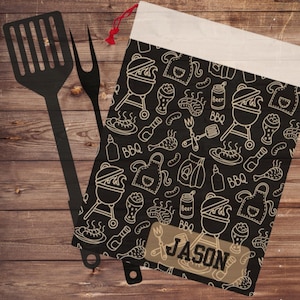 May include: A black canvas bag with a white drawstring and a white border. The bag is decorated with a black and white pattern of grilling and barbecue related items. The bag has a brown label with the name "JASON" printed on it.